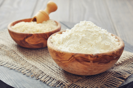 Raw rice and flour in bowls on wooden background